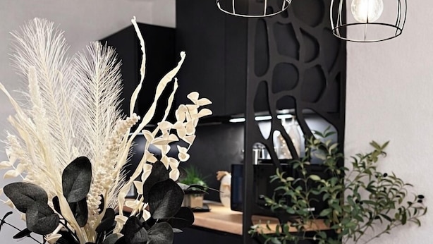 Een eetruimte met een houten tafel, een geweven tafelonderzetter, een decoratieve vaas met begroeiing en hanglampen.