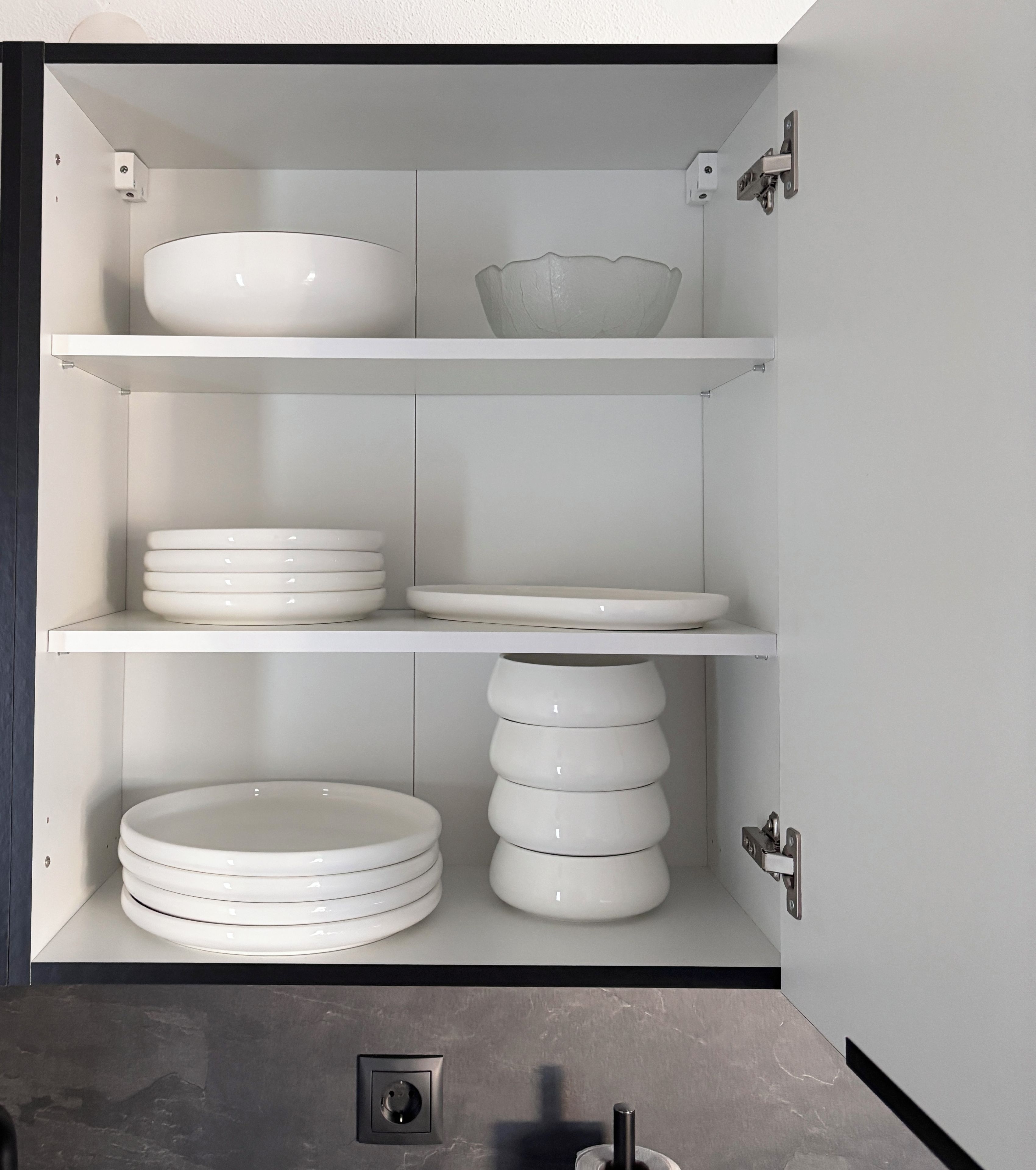 A kitchen cabinet with white shelves holding plates and bowls.