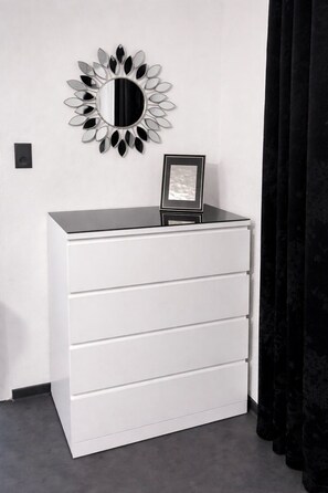 A white dresser with a mirror and a picture frame on top, against a white wall with a black curtain. - Ferienhaus Schieferland - Your vacation home between the Moselle and the Nürburgring (Müllenbach)
