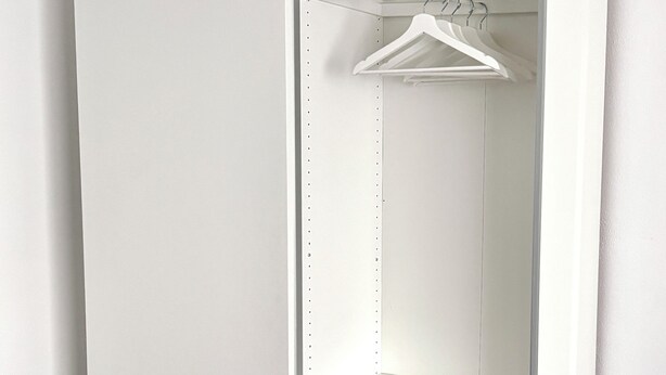 Un dressing blanc avec des portes ouvertes, comprenant un espace pour suspendre les vêtements et des étagères en fil métallique.