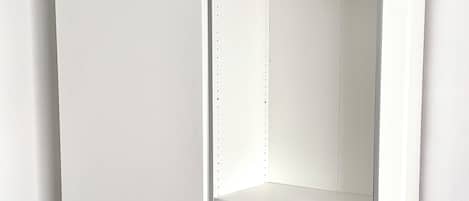 Un dressing blanc avec des portes ouvertes, comprenant un espace pour suspendre les vêtements et des étagères en fil métallique.