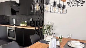 Een moderne keuken met zwarte kastjes, een houten aanrecht en een eethoek, gedekt met witte borden, glazen en een vaas witte bloemen.