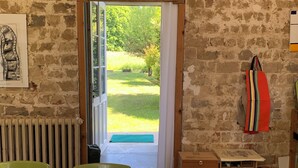 A room with a brick wall, a table with chairs, a radiator, and a view of a garden through an open door. - Family home (Bussus-lès-Yaucourt)
