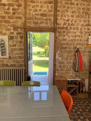 A room with a brick wall, a table with chairs, a radiator, and a view of a garden through an open door. - Family home (Bussus-lès-Yaucourt)