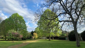 A well-maintained grassy area with mature trees, a clear sky, and a building in the background. - Family home (Bussus-lès-Yaucourt)