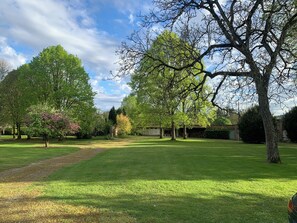 A well-maintained grassy area with mature trees, a clear sky, and a building in the background. - Family home (Bussus-lès-Yaucourt)