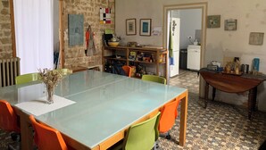 A dining area with a glass table, orange and green chairs, a brick wall, and a kitchen in the background. - Family home (Bussus-lès-Yaucourt)