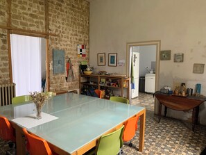 A dining area with a glass table, orange and green chairs, a brick wall, and a kitchen in the background. - Family home (Bussus-lès-Yaucourt)