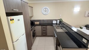 Uma cozinha com geladeira, fogão, pia e um relógio na parede.