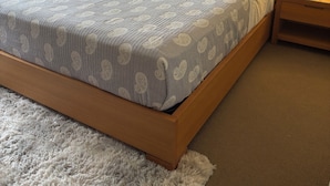 Uma cama bem arrumada com roupa de cama estampada, um tapete fofo, uma pintura de peixes na parede e um abajur.