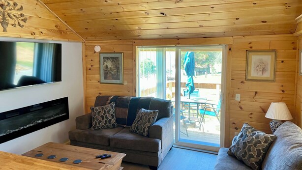 A wooden interior with a sofa, a coffee table, a TV, and a sliding glass door leading to an outdoor area. - 3-bedroom cabin in Madisonville TN (Madisonville)