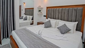 Una cama bien hecha con almohadas, una mesita de noche, un espejo y una lámpara de pared.