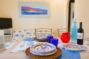 Una mesa de comedor dispuesta con platos, una jarra roja, vasos azules y botellas de vino.