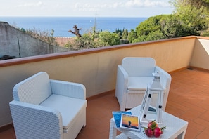 Ein Balkon mit zwei weißen Korbstühlen, einem kleinen Tisch und einem Buch mit dem Titel 'ELBA'.