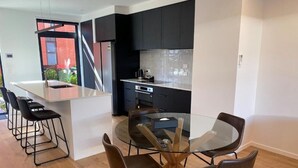 A modern kitchen with black cabinets, a stainless steel island, and a glass dining table with chairs. - Merivale Executive Stays (Christchurch)