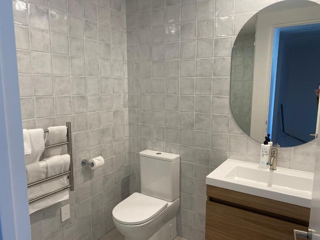 A bathroom with a toilet, a towel rack, a sink, and a mirror.