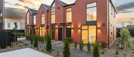 A modern residential building with a brick facade, large windows, and a well-maintained garden.
