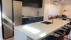 A modern kitchen with a central island, dark cabinetry, and a built-in oven. - Merivale Executive Stays (Christchurch)