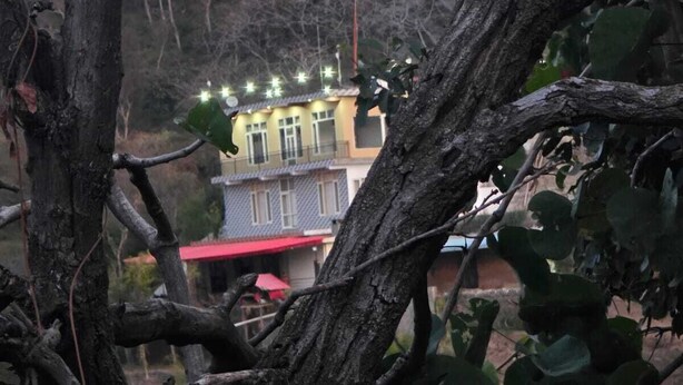 A building with multiple windows and a red roof, surrounded by trees and hills. - ShantiKunj Homestay Nearby Morni Hills Waterfall (Panchkula)