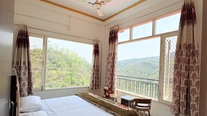 A bedroom with a bed, a desk, a chair, a ceiling fan, and large windows with curtains. - ShantiKunj Homestay Nearby Morni Hills Waterfall (Panchkula)