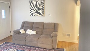 A living room with a gray sofa, a patterned rug, and a zebra print artwork on the wall. - Spacious 4-bedroom apartment near Mayo Clinic (Rochester)