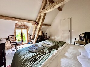 A bedroom with a sloped ceiling, a bed with a green blanket, a chair, a desk, and a door. - The charm of a family and country home (Longny les Villages)