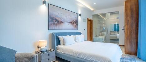 Une chambre à coucher moderne avec un grand lit, une table de chevet, un tableau accroché au mur et un ventilateur de plafond.