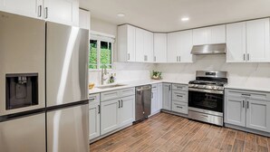 A modern kitchen with white cabinets, stainless steel appliances, and a wooden floor. - Serene 4 bedroom house with AC in charming Tacoma (Tacoma)