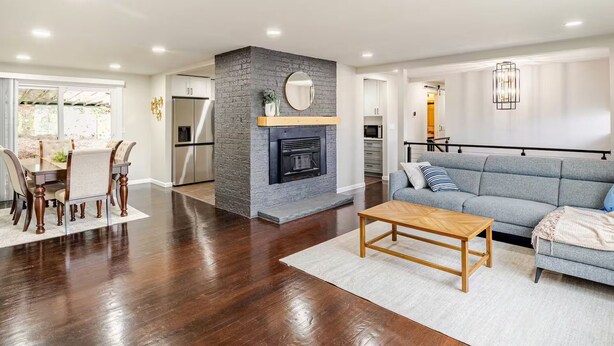A modern living room with a fireplace, a dining area with a table and chairs, a kitchen in the background, and a gray sofa with a throw blanket. - Serene 4 bedroom house with AC in charming Tacoma (Tacoma)