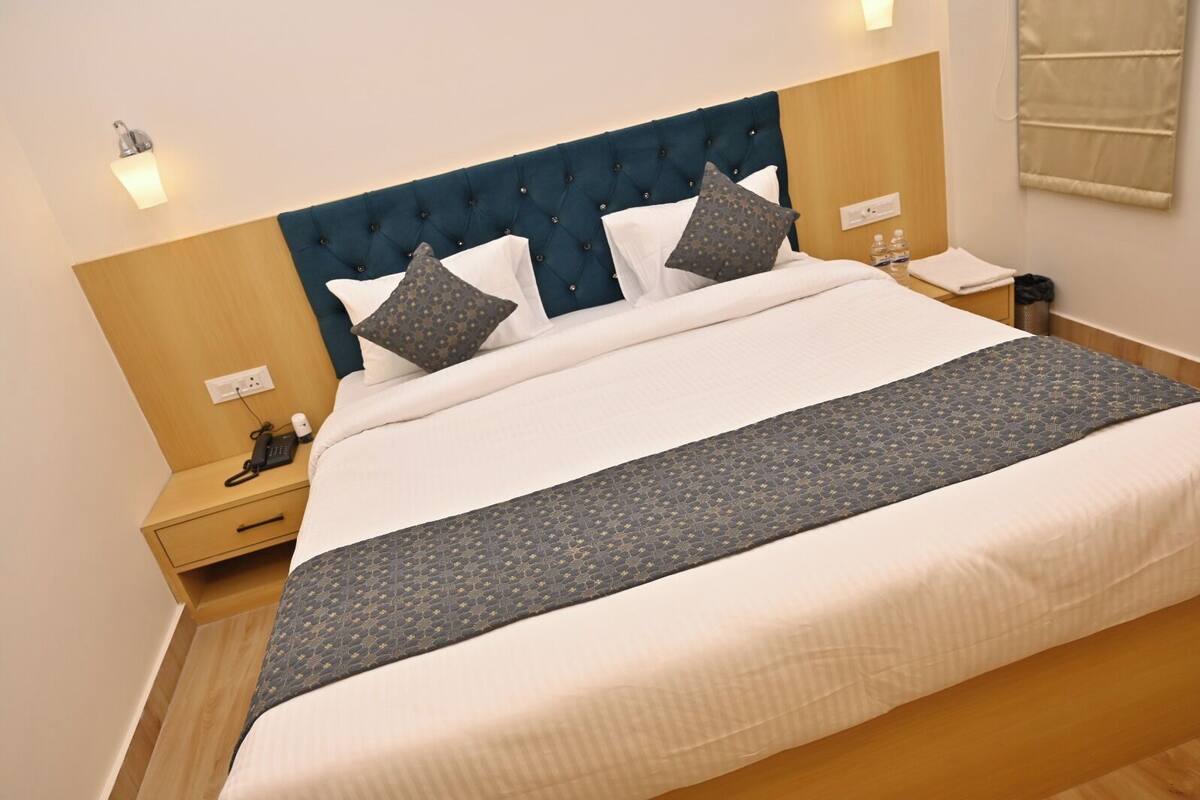 A hotel room with a large bed, a wooden headboard, bedside tables with lamps, and a wall-mounted phone.