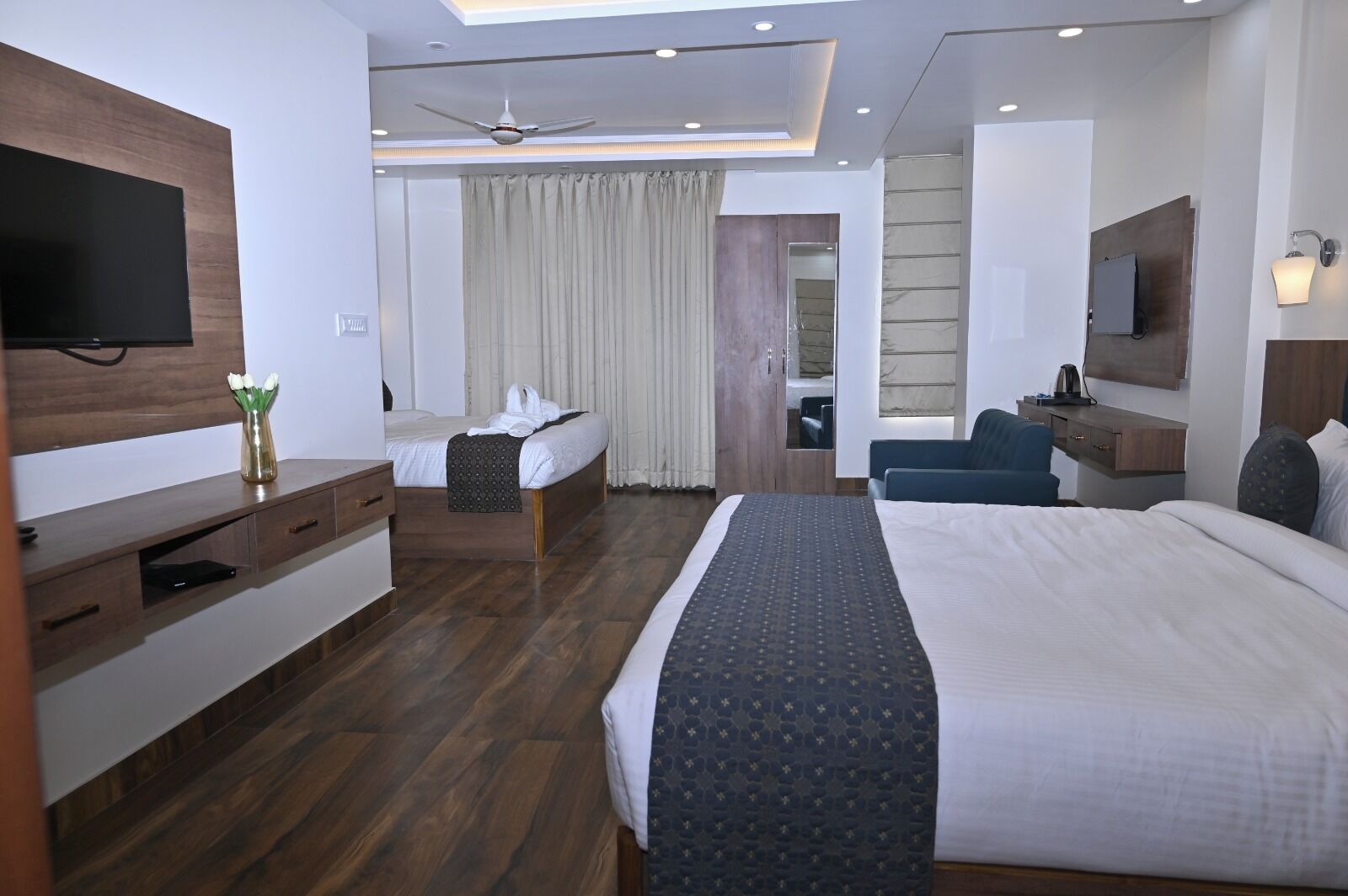Ein modernes Hotelzimmer mit einem großen Bett, einem Schreibtisch, einem Sessel, einem Fernseher und einem Deckenventilator.