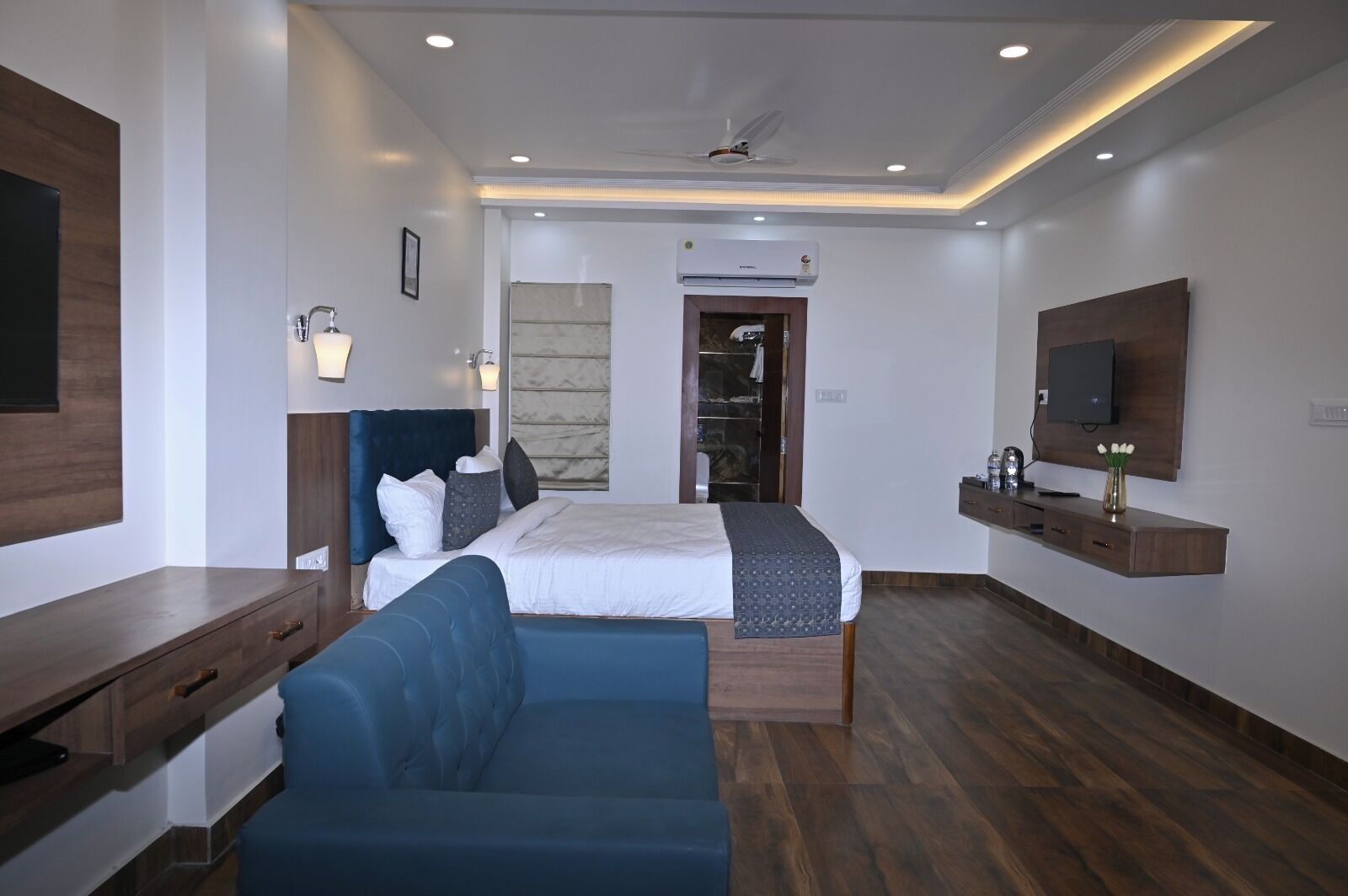 A modern hotel room with a bed, a seating area, a TV, and a wardrobe.