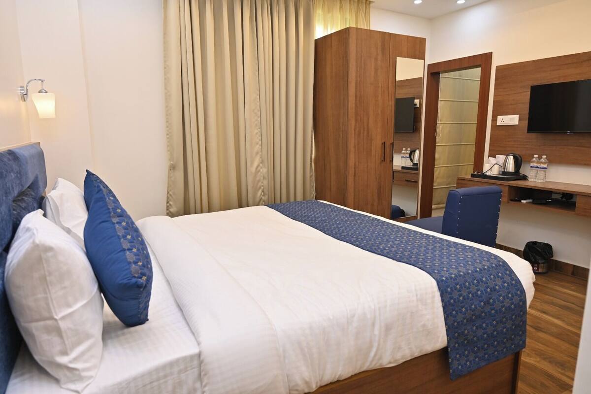 A hotel room with a bed, a desk with a chair, a TV, and a wardrobe.