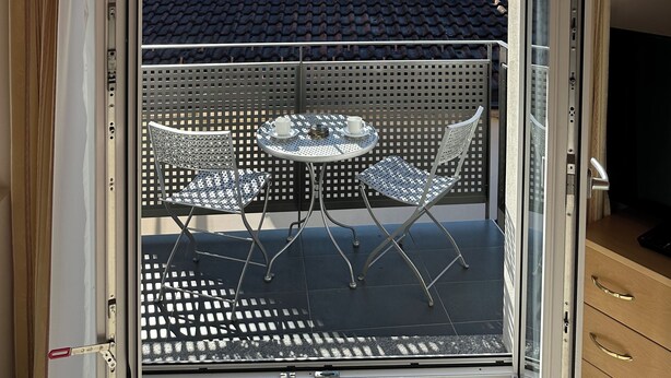 Ein Balkon mit Tisch und Stühlen, einem Fernseher und Blick auf Berge und Wasser.