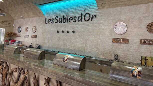 Uma receção com design moderno, uma parede com textura ondulada e um letreiro que diz 'Les Sables d'Or'.