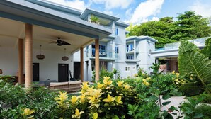 A multi-story residential building with balconies, a covered porch, and lush greenery.