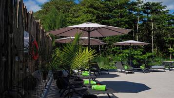 A poolside area with lounge chairs, umbrellas, and a bamboo fence.
