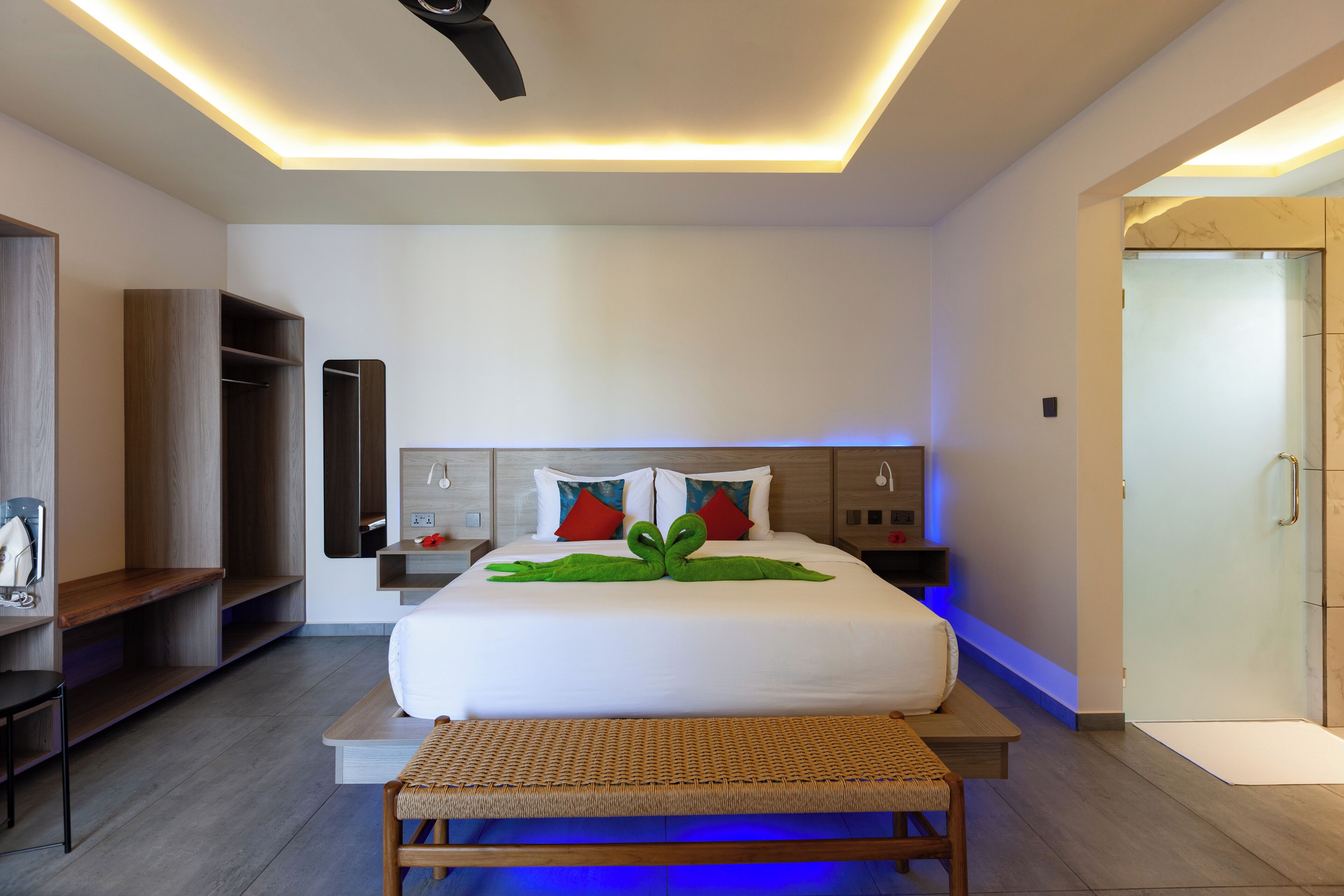 A modern hotel room with a large bed, bedside tables, a wardrobe, and a shower area.