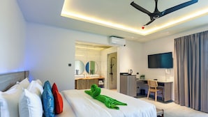A hotel room with a bed, pillows, a desk, a chair, a television, and a ceiling fan.