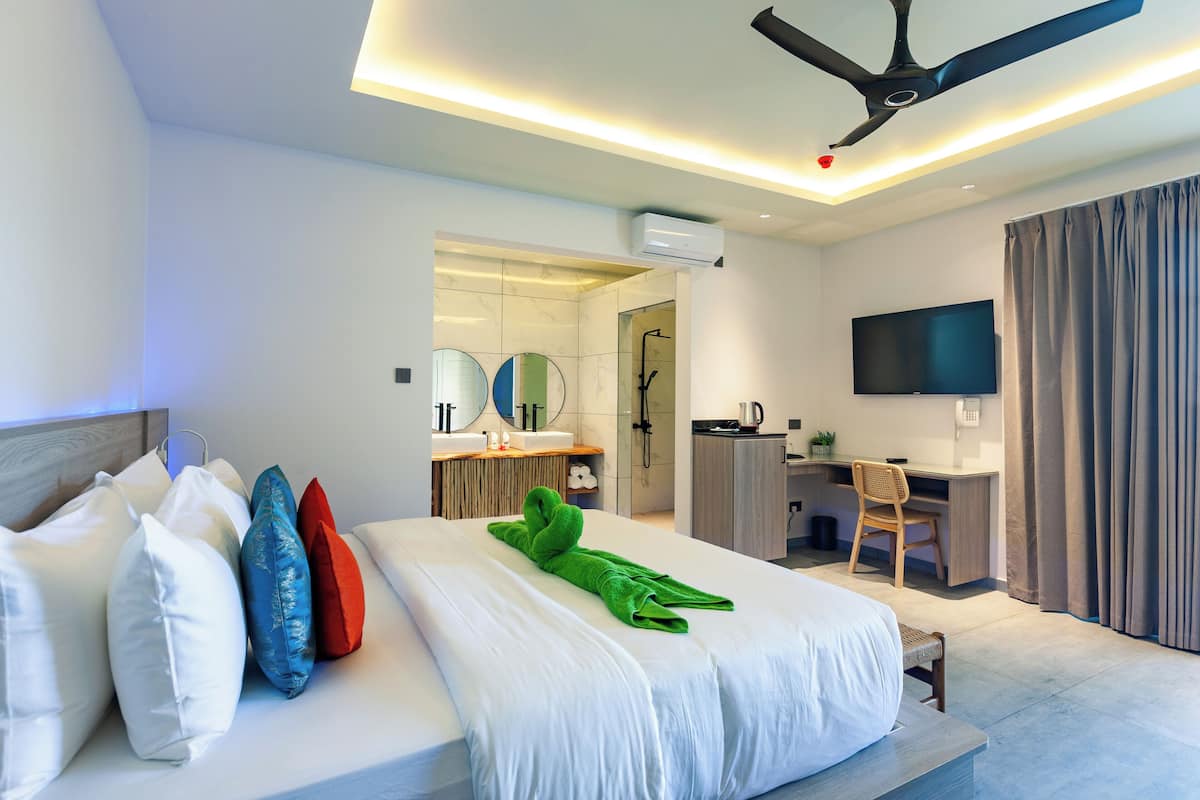 Ein Hotelzimmer mit einem Bett, Kissen, Schreibtisch, Stuhl, Fernseher und Deckenventilator.