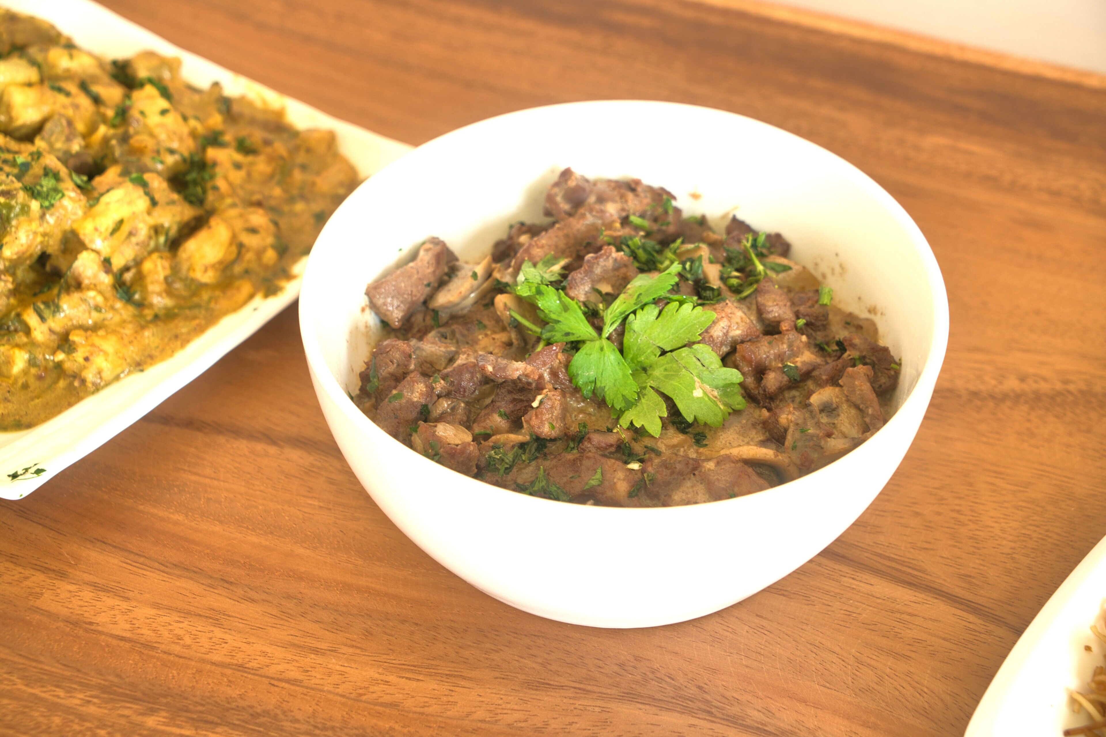Uma tigela branca de comida decorada com salsa sobre uma mesa de madeira.