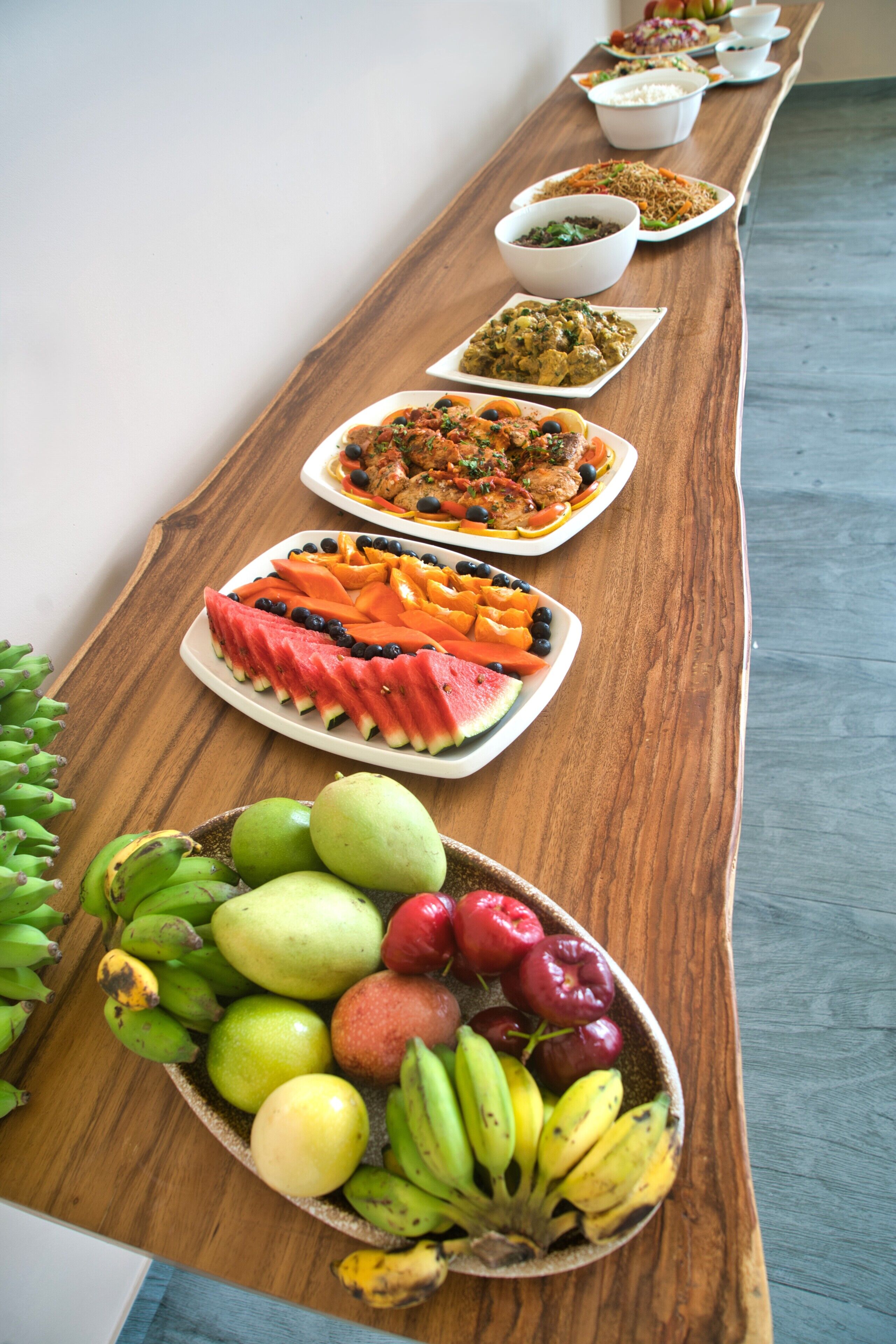 A long wooden table with various dishes and fruits arranged on it.