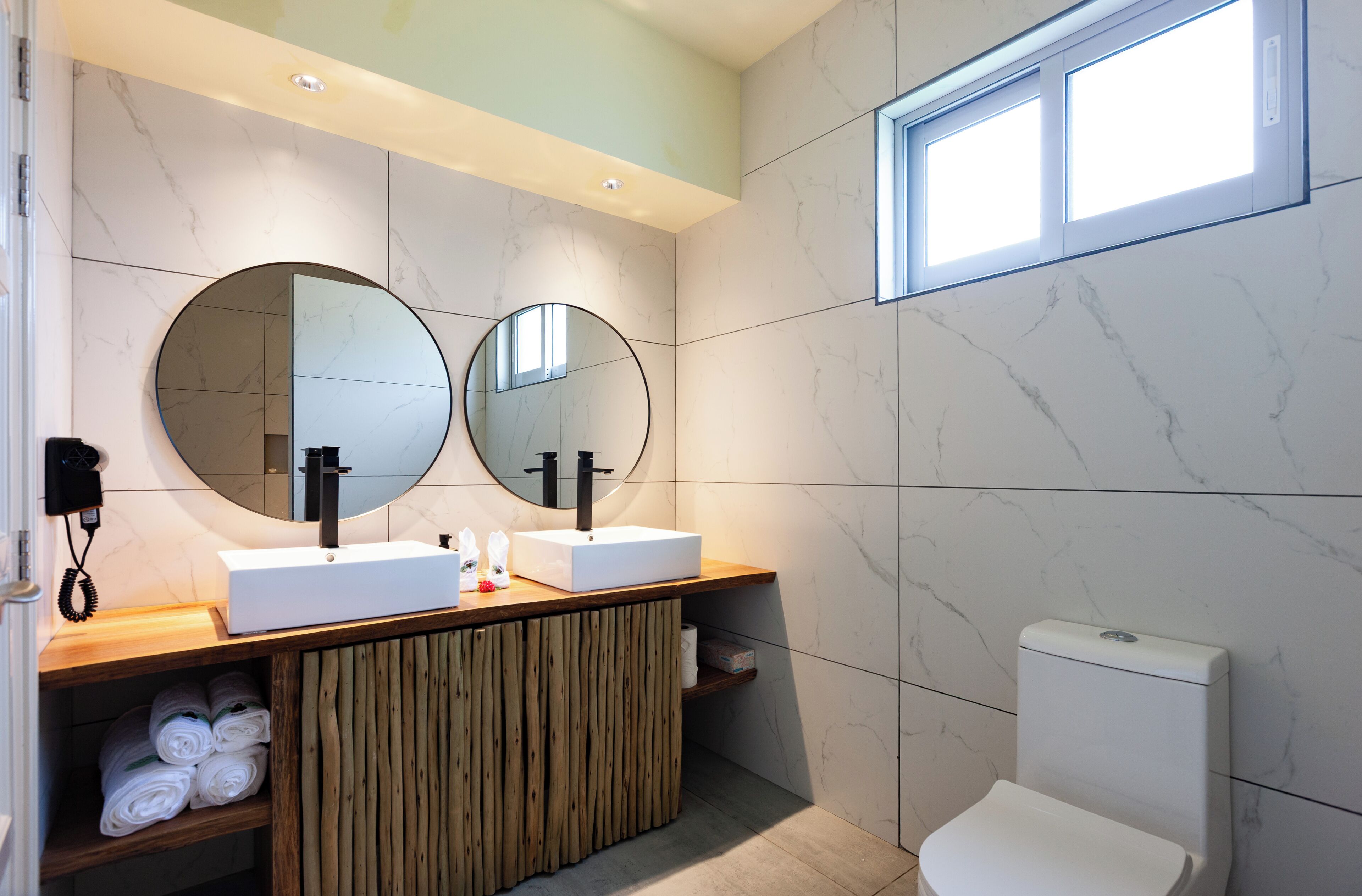 A modern bathroom with two sinks, a mirror, a toilet, and a wooden vanity.