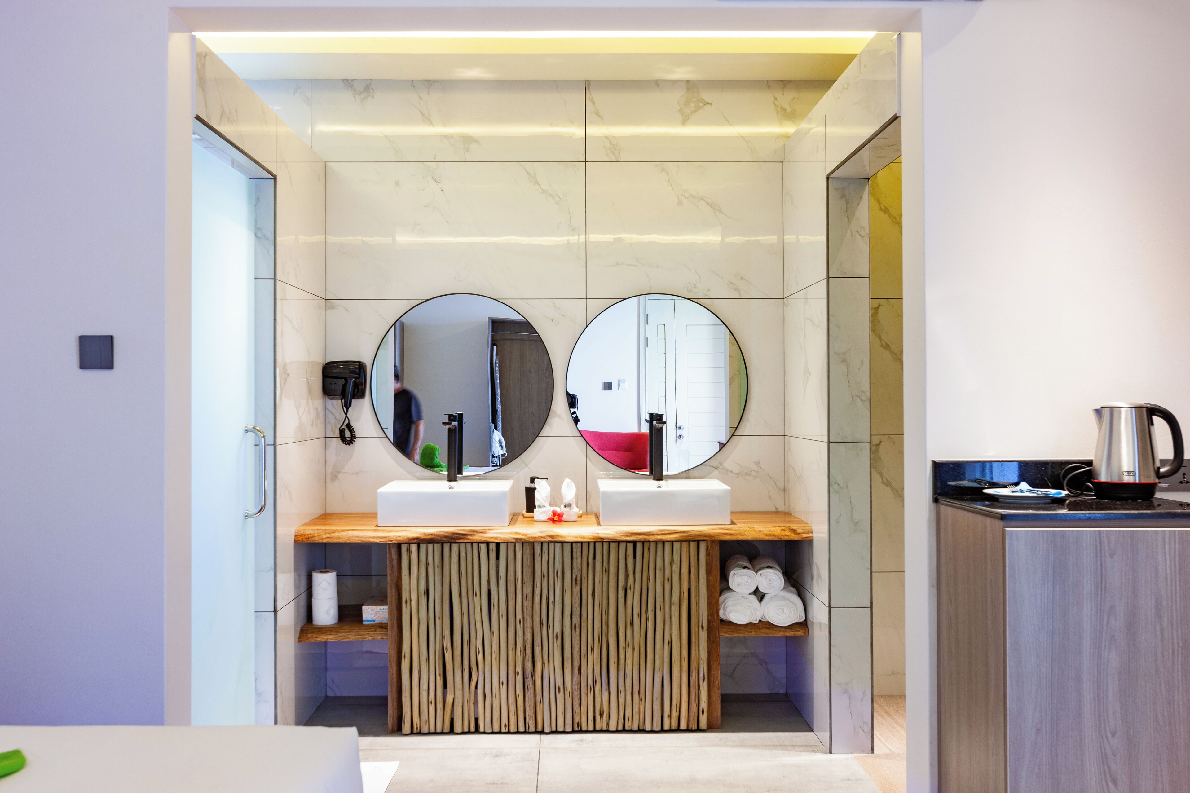 A modern bathroom with two sinks, a wooden vanity, and a coffee maker.