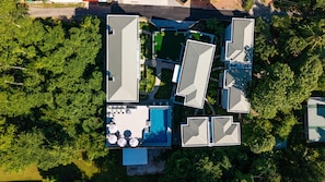 An aerial view of a resort with multiple buildings, a swimming pool, and surrounding greenery.