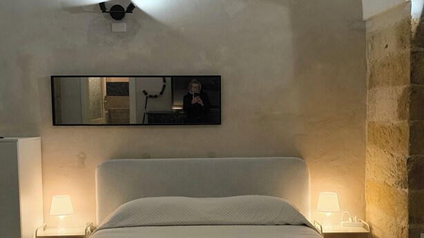 Ein Schlafzimmer mit einem Bett, zwei Nachttischlampen, einem Deckenventilator, einem Spiegel und einer Steinwand.