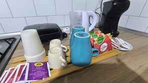 Eine Küchenarbeitsplatte mit verschiedenen Gegenständen, darunter eine Kaffeemaschine, Tassen, eine Kanne und verpackten Lebensmitteln.