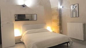 Ein Schlafzimmer mit Bett, Kommode, Spiegel, Heizkörper und Wandlampe.
