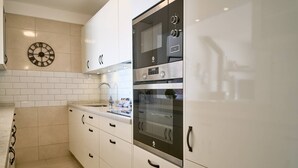 Una cocina con armarios blancos, horno de acero inoxidable, un reloj de pared y salpicadero de azulejos.