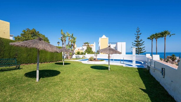 Un área exterior bien cuidada con piscina, sombrillas y un banco.